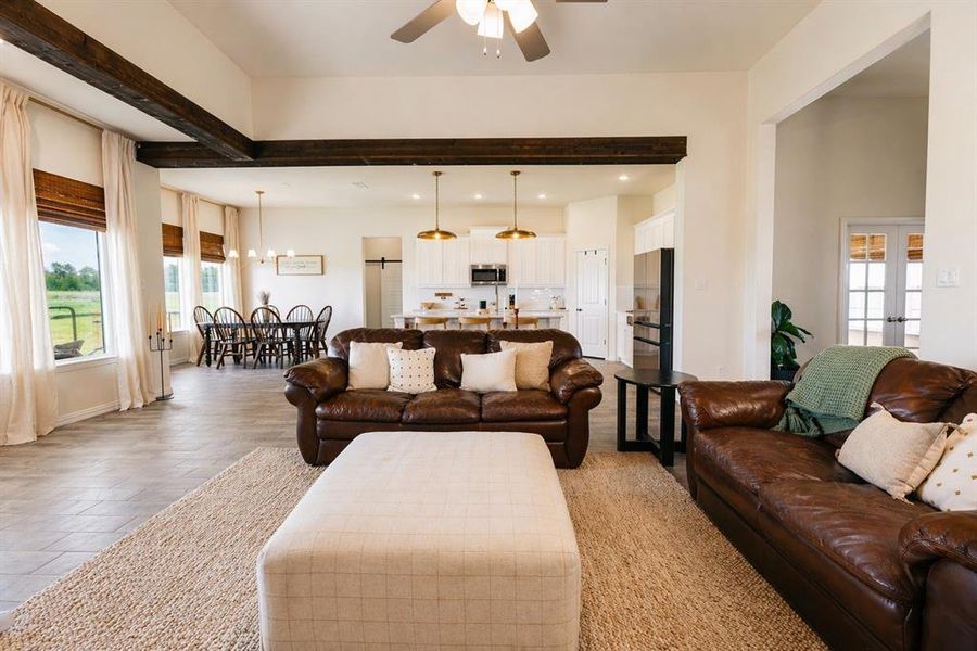 Spacious living area featuring exposed wood beams, vaulted ceilings, tile flooring, and multiple windows with natural light