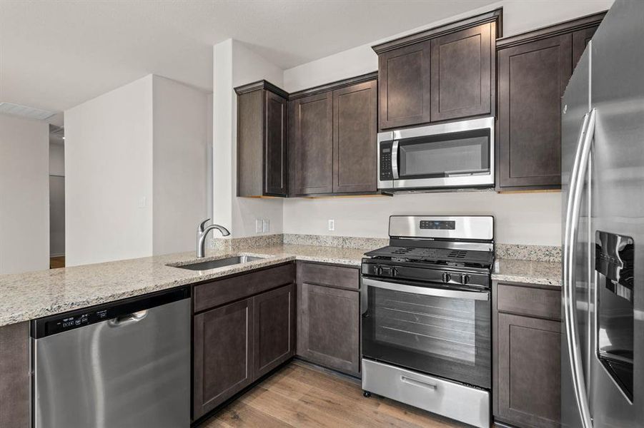 Kitchen featuring stainless steel appliances, light wood-style flooring, dark brown cabinetry, light stone countertops, and a peninsula