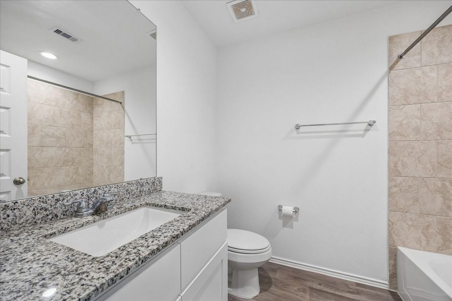 Secondary bathroom with granite countertop, undermount sink, a large mirror, and a tub-shower combo.
