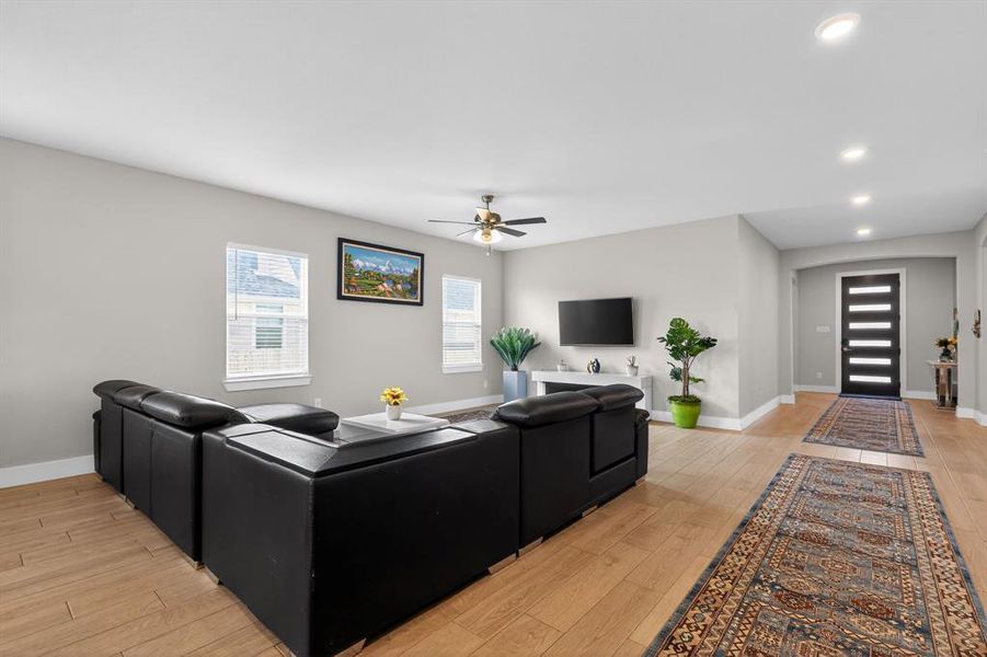 The open concept living area features light wood flooring, recessed lighting, and a ceiling fan