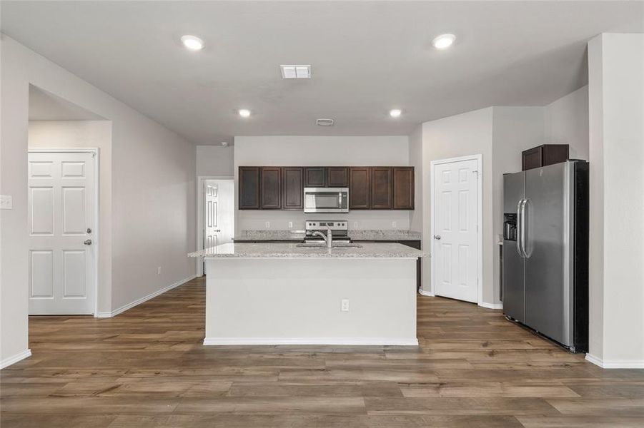 Kitchen with stainless steel appliances, dark brown cabinetry, dark wood-style flooring, recessed lighting, and an island with sink Kitchen with stainless steel appliances, dark brown cabinetry, dark wood-style flooring, recessed lighting, and an island with sink