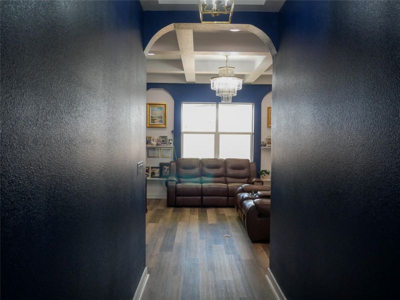 Hall with coffered ceiling, suspended lighting, arched walkways, a textured wall, and dark wood finished floors
