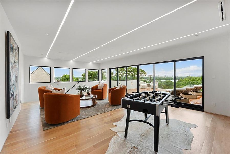 Spacious entertainment room featuring recessed linear lighting, light wood-finish flooring, and expansive sliding glass doors
