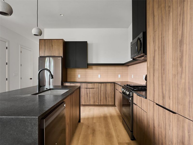 Kitchen with a center island with sink, black appliances, decorative light fixtures, modern cabinets, and dark stone counters Kitchen with a center island with sink, black appliances, decorative light fixtures, modern cabinets, and dark stone counters