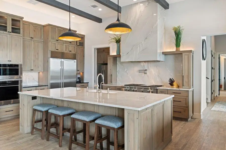 The chef’s kitchen is highlighted by a stunning marble vent hood and custom wood cabinetry, while the kitchen island provides seating for four under designer pendant lighting.