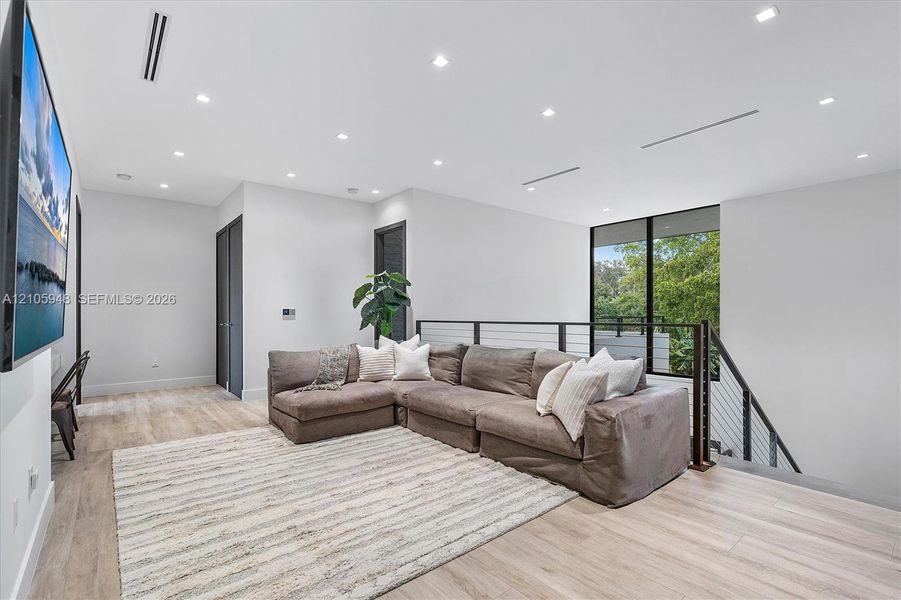 Open-concept space featuring light wood-finish flooring, recessed ceiling lighting, linear HVAC diffusers, and a staircase with a horizontal cable railing system