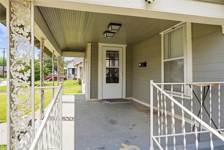 Inviting front porch featuring decorative metalwork railings, a white paneled door with glass inserts, and horizontal siding