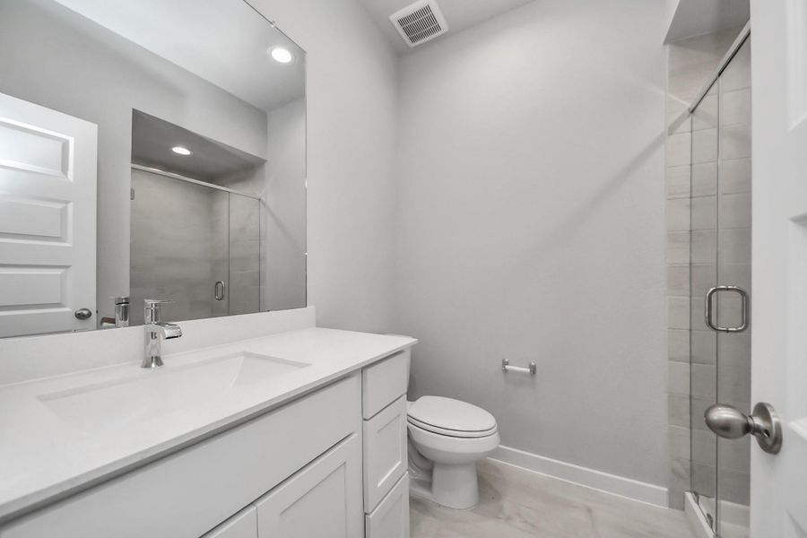 Secondary bath features tile flooring, walk-in shower with tile surround, light stained wood cabinets, beautiful light countertop.