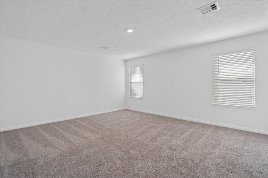 Relax and recharge in this stunning primary suite! This expansive room offers plush carpeting, neutral-toned walls, high ceilings, recessed lighting, large windows fitted with privacy blinds, and an added sitting area—perfect for unwinding after a long day.