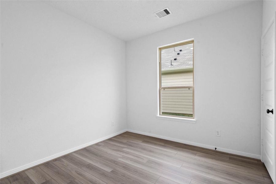 This secondary bedroom offers comfort and style with vinyl plank flooring, neutral paint tones, recessed lighting, a large window, and a generously sized closet
