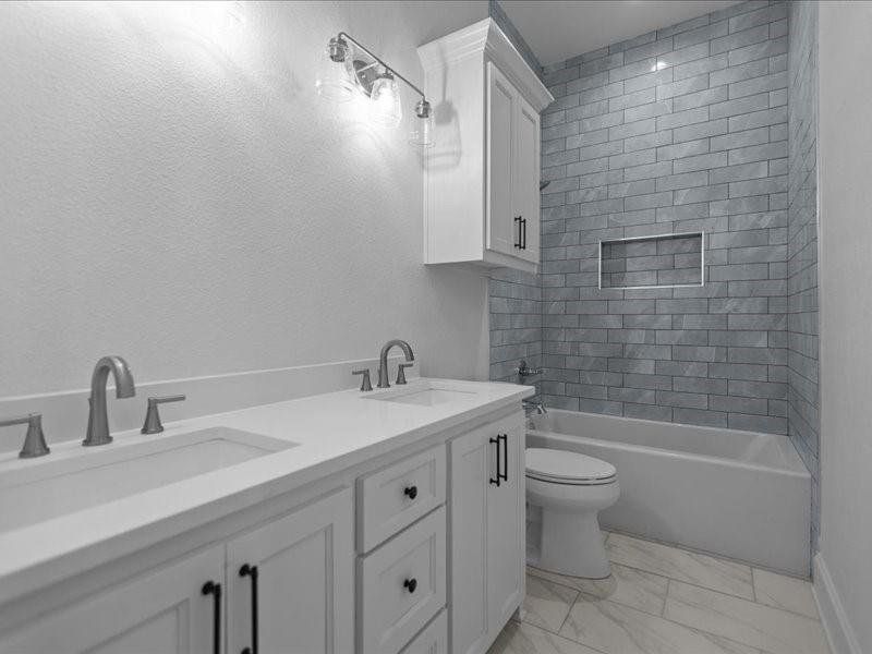 Bathroom featuring double vanity, shower / bath combination, and light marble finish flooring