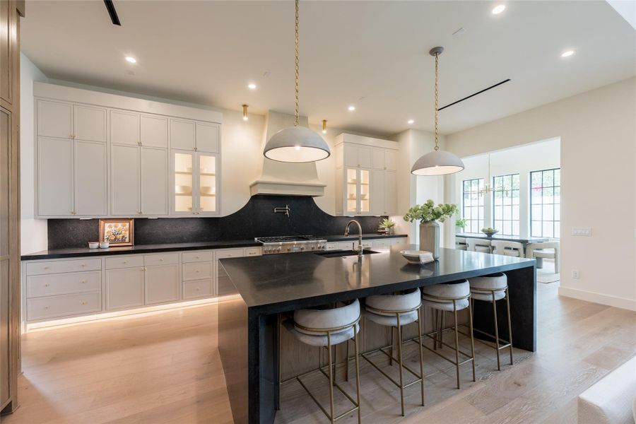 The kitchen is a masterclass in sculpted elegance, featuring a custom-plastered lime wash vent hood with graceful curves, backlit brass-trimmed mesh panels, and unlacquered brass hardware that will develop a rich patina over time. Soft cream cabinetry and mood lighting—from under-cabinet illumination—create warmth and contrast against the dramatic black stone countertops and oversized double waterfall island centerpiece. The kitchen is a masterclass in sculpted elegance, featuring a custom-plastered lime wash vent hood with graceful curves, backlit brass-trimmed mesh panels, and unlacquered brass hardware that will develop a rich patina over time. Soft cream cabinetry and mood lighting—from under-cabinet illumination—create warmth and contrast against the dramatic black stone countertops and oversized double waterfall island centerpiece.