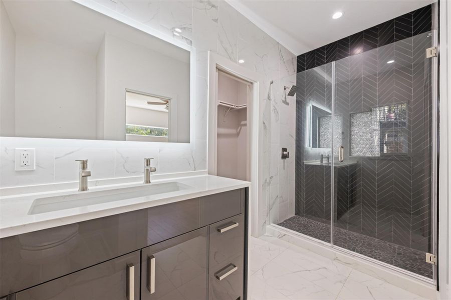 Full bath featuring light marble finish floors, vanity, a marble finish shower, recessed lighting, and a walk in closet