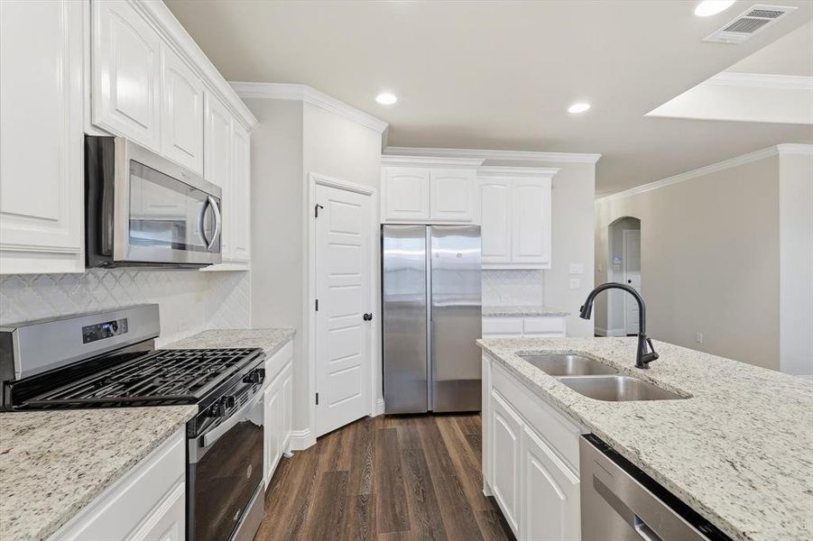 Kitchen featuring stainless steel appliances, arched walkways, light stone countertops, recessed lighting, and dark wood-type flooring