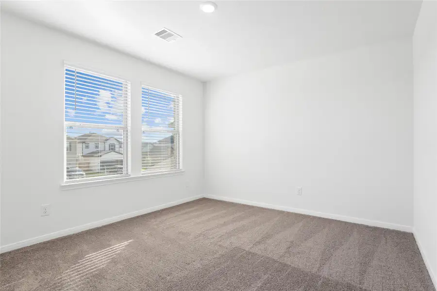This secondary bedroom offers comfort and style with plush carpeting, neutral paint tones, recessed lighting, a large window with blinds, and a generously sized closet.