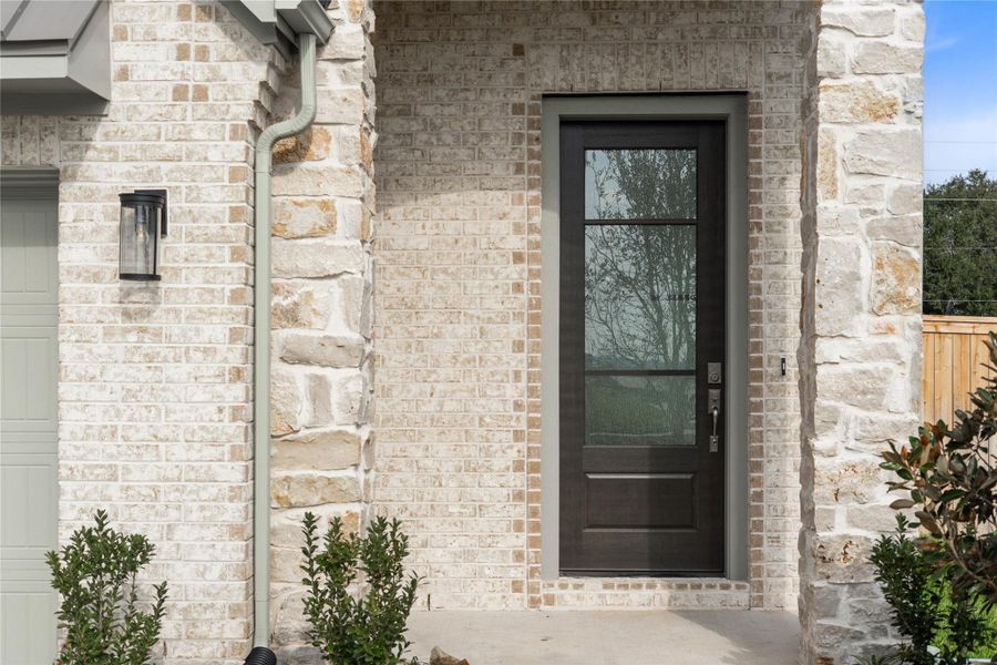 As you walk up to this beautiful home, you notice the stone and brick elevation with contemporary black wall sconce light fixture. The inviting front door is accentuated by a brass-toned handle set contributing to the strong curb appeal.