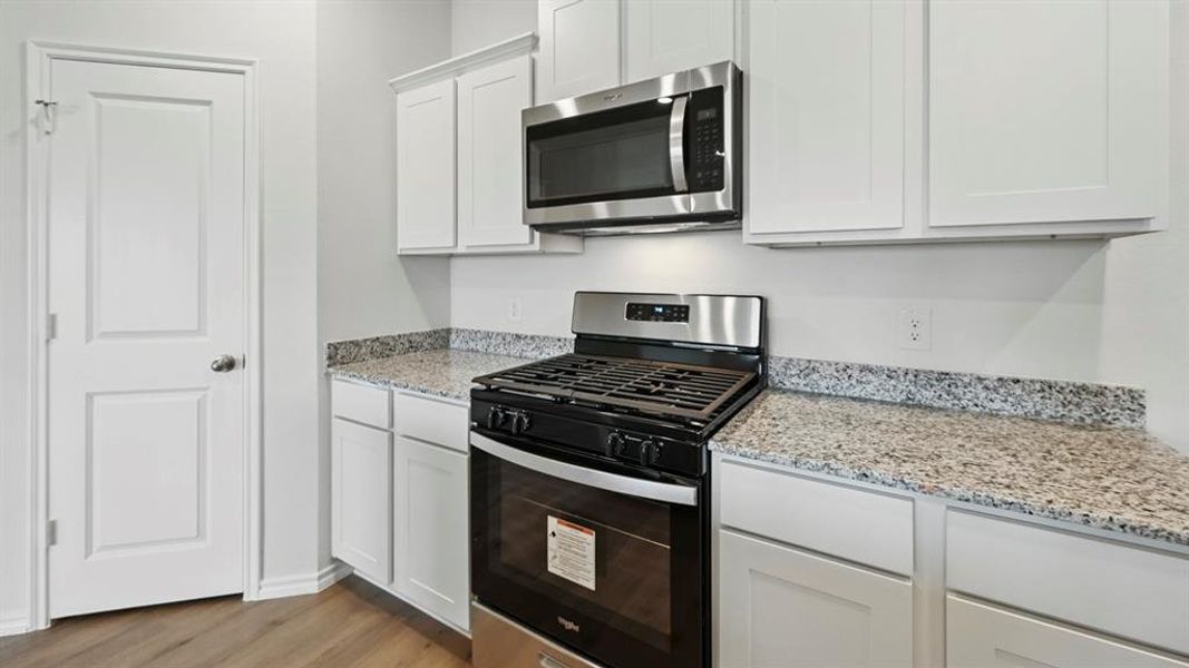 Kitchen featuring appliances with stainless steel finishes, light stone countertops, white cabinets, and light wood-style floors