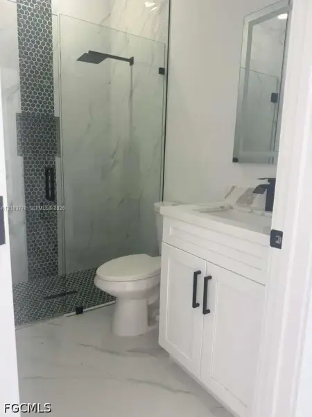 Bathroom featuring a white vanity with matte black hardware, a walk-in shower with glass enclosure, oversized wall and floor tiles, mosaic tile shower accents, and a rainfall showerhead Bathroom featuring a white vanity with matte black hardware, a walk-in shower with glass enclosure, oversized wall and floor tiles, mosaic tile shower accents, and a rainfall showerhead