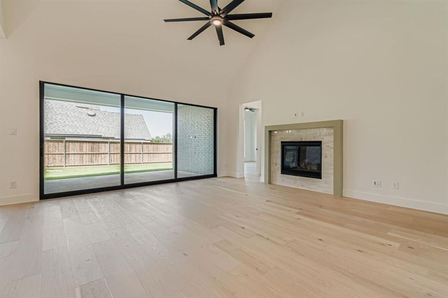Unfurnished living room featuring high vaulted ceiling, light wood-style floors, a tiled fireplace, and a ceiling fan Unfurnished living room featuring high vaulted ceiling, light wood-style floors, a tiled fireplace, and a ceiling fan