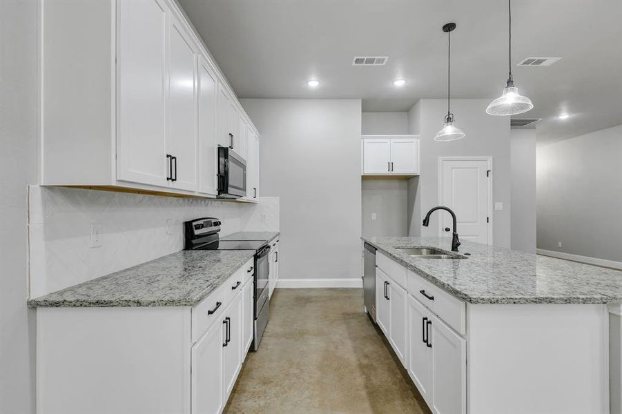 Kitchen with concrete flooring, appliances with stainless steel finishes, light stone counters, a kitchen island with sink, and hanging light fixtures