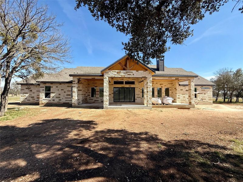Rear view of house featuring a patio, a chimney, and stone siding