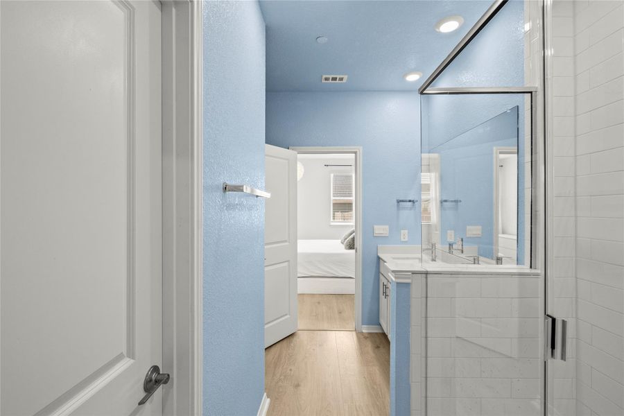 A well-lit bathroom with light blue walls and hardwood-style flooring offers a seamless transition to the adjacent bedroom.