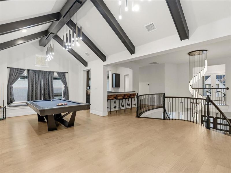 Open entertainment area with vaulted ceilings, exposed dark beams, and light wood-finish flooring Open entertainment area with vaulted ceilings, exposed dark beams, and light wood-finish flooring