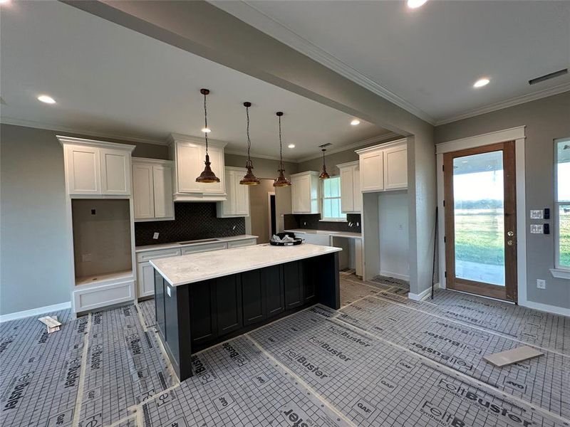 Kitchen featuring white cabinetry, a center island, hanging light fixtures, decorative backsplash, and ornamental molding