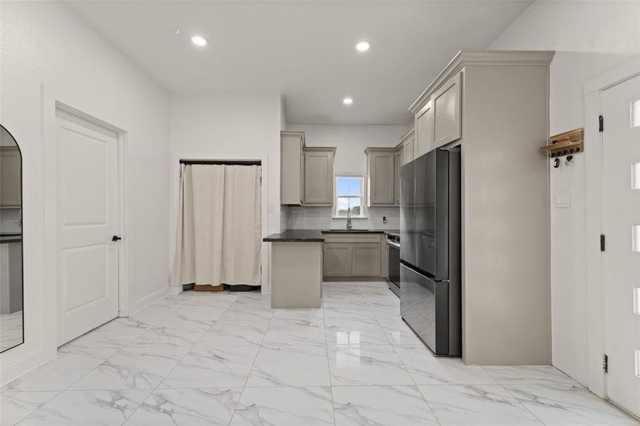 Kitchen with freestanding refrigerator, light marble finish flooring, recessed lighting, arched walkways, and gray cabinetry