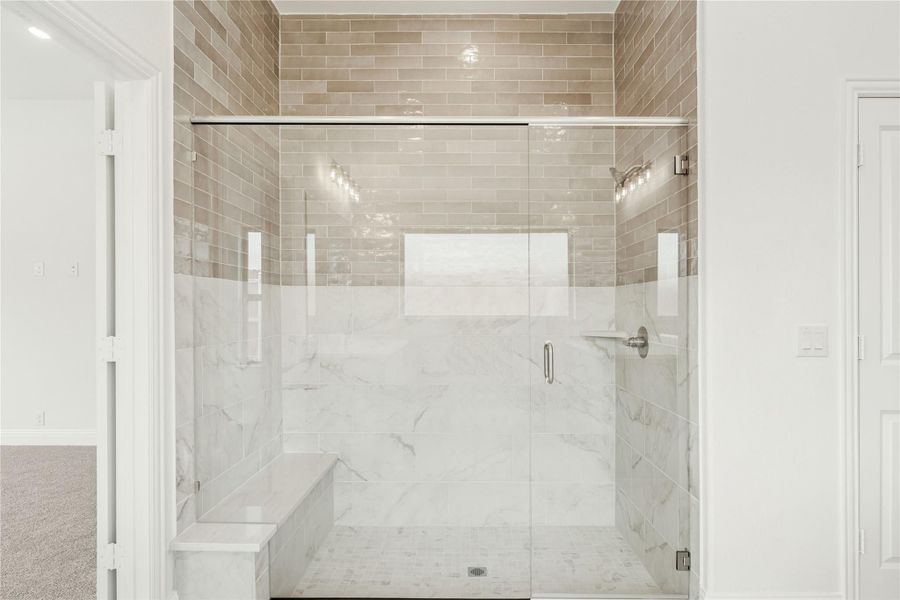 Walk-in shower with glass doors, marble tile walls, built-in bench, and beige subway tile accent wall above