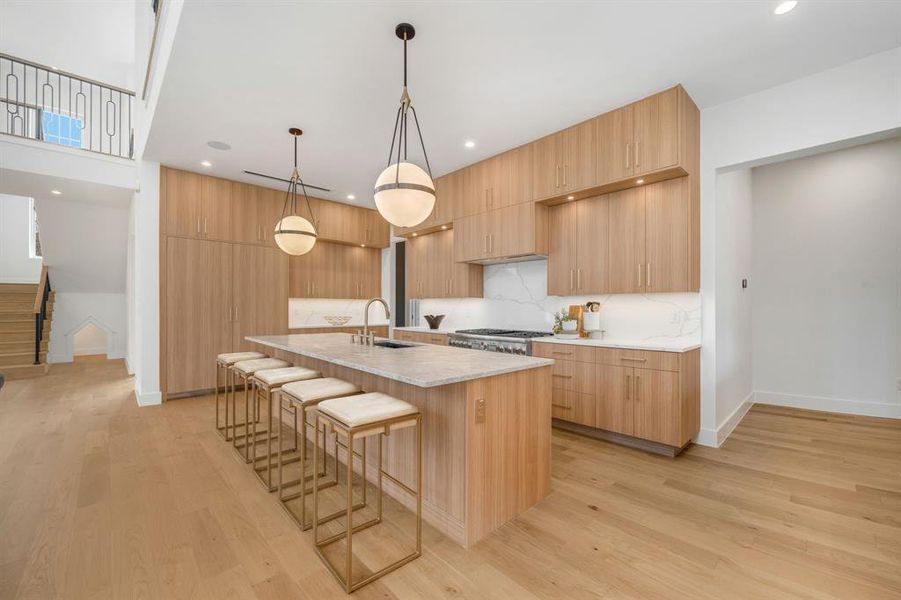 Kitchen with a breakfast bar area, modern cabinets, pendant lighting, light stone countertops, and a center island with sink Kitchen with a breakfast bar area, modern cabinets, pendant lighting, light stone countertops, and a center island with sink