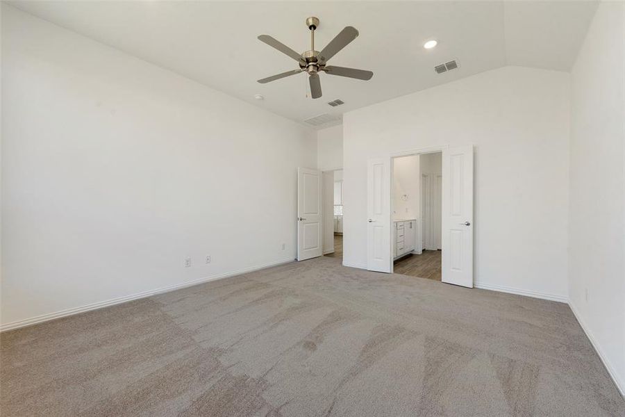 Unfurnished bedroom featuring ceiling fan, ensuite bath, vaulted ceiling, and carpet