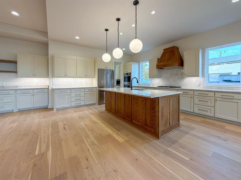 Open-concept kitchen featuring a large wood-paneled island with a stone countertop, light wood-finish flooring, and pendant lighting