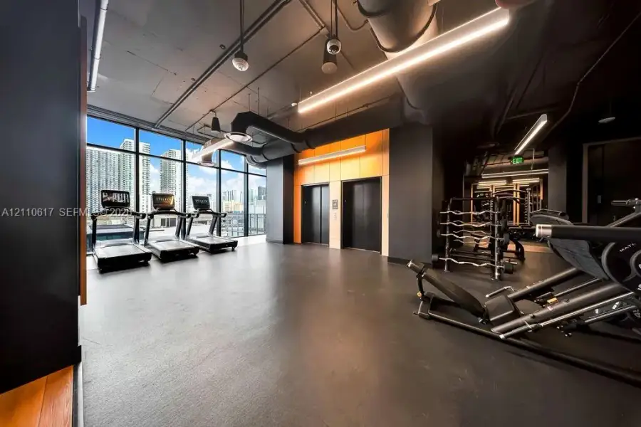 Fitness area featuring floor-to-ceiling windows, exposed industrial-style ductwork, high ceilings, rubberized flooring, and dual elevator access Fitness area featuring floor-to-ceiling windows, exposed industrial-style ductwork, high ceilings, rubberized flooring, and dual elevator access