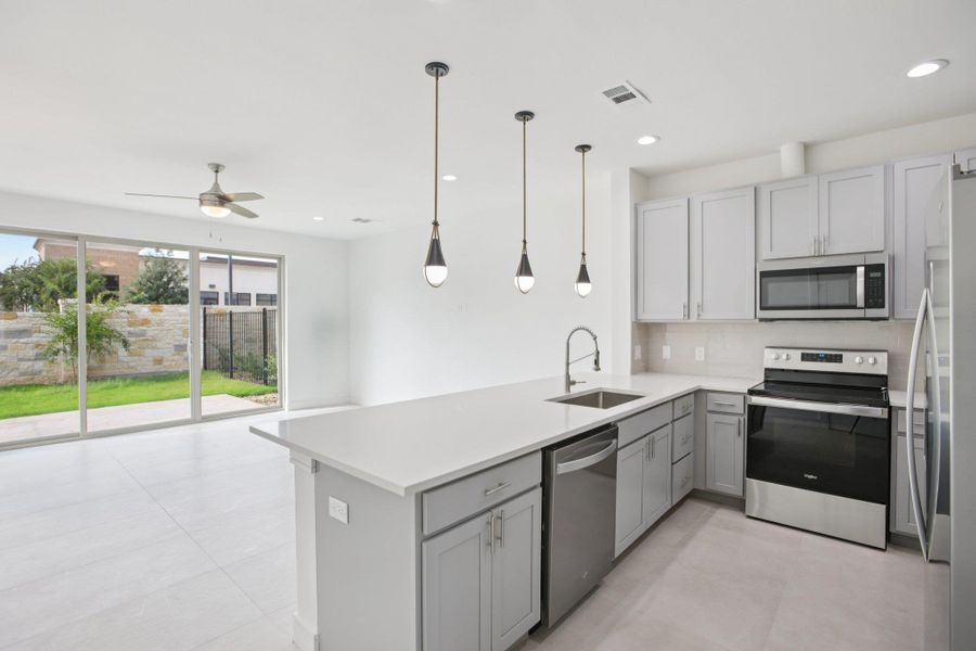 Kitchen with stainless steel appliances, gray cabinets, a peninsula, tasteful backsplash, and light stone countertops