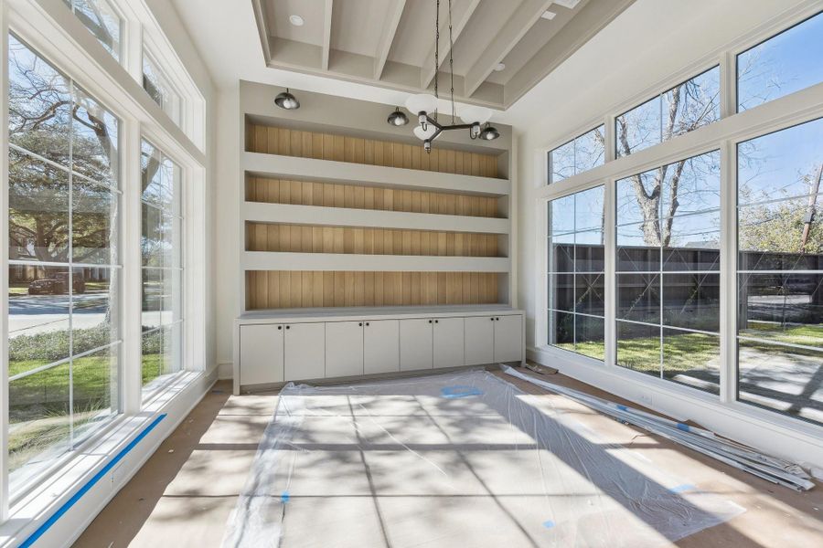 Located off the entrance of the home is a study with built-in shelving and cabinets.  The ceiling has painted beams and there are windows on both the north and south side of the room.