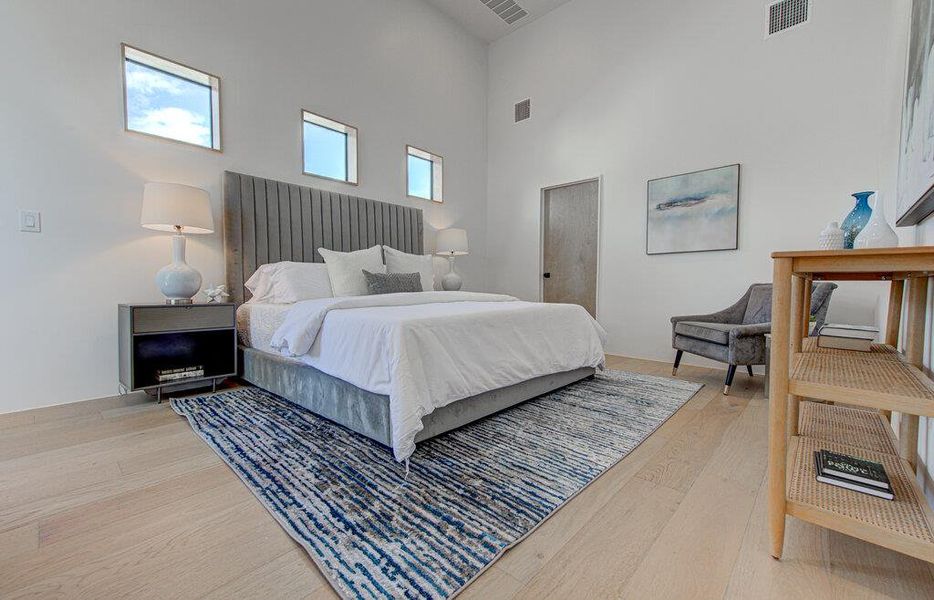 Bedroom featuring light wood-type flooring, visible vents, and a high ceiling