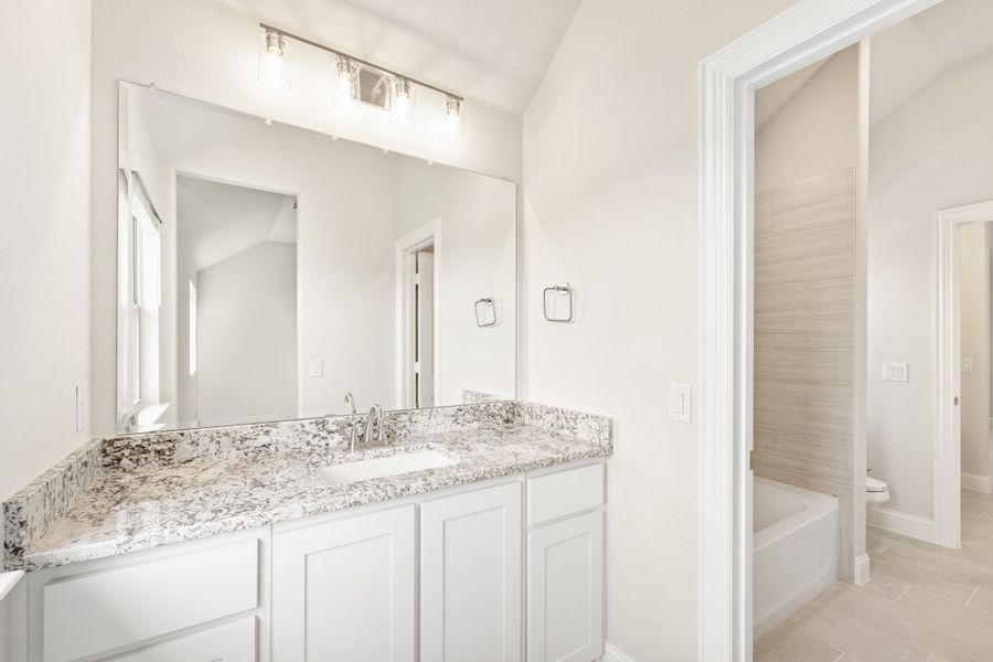 Bathroom with white vanity, granite countertop, large mirror, and soaking tub visible through doorway