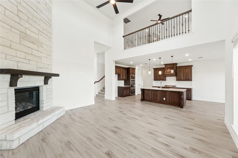 Open living area with stone fireplace, high ceilings, and open kitchen with dark wood cabinets and island Open living area with stone fireplace, high ceilings, and open kitchen with dark wood cabinets and island