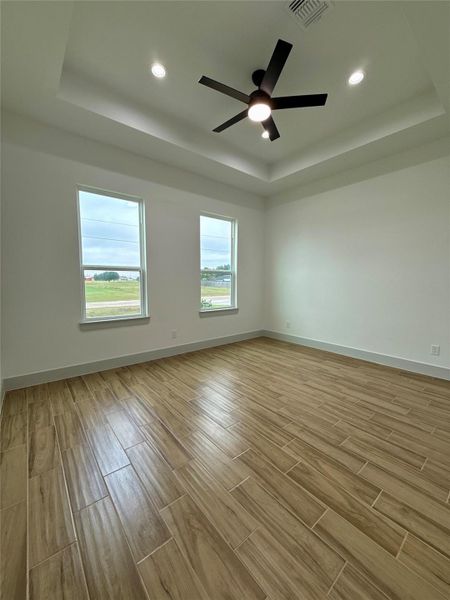 This room features wood-look tile flooring and a modern ceiling fan. It has two large windows providing ample natural light and a tray ceiling with recessed lighting. The walls are painted in a neutral tone, offering a bright and airy atmosphere. This room features wood-look tile flooring and a modern ceiling fan. It has two large windows providing ample natural light and a tray ceiling with recessed lighting. The walls are painted in a neutral tone, offering a bright and airy atmosphere.