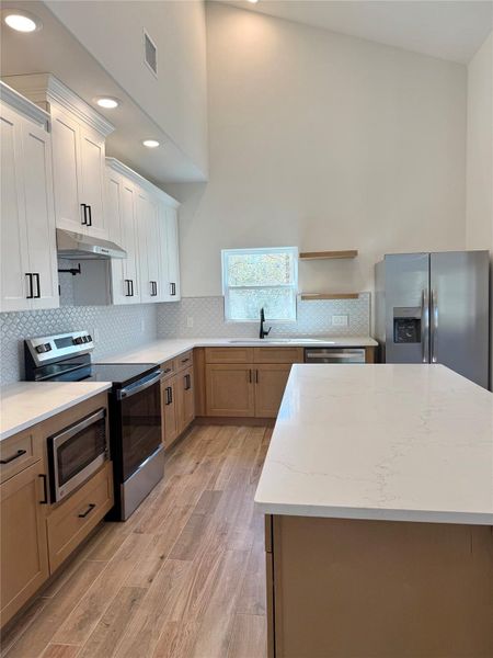 Kitchen featuring appliances with stainless steel finishes, a center island, light wood-type flooring, light stone counters, and under cabinet range hood