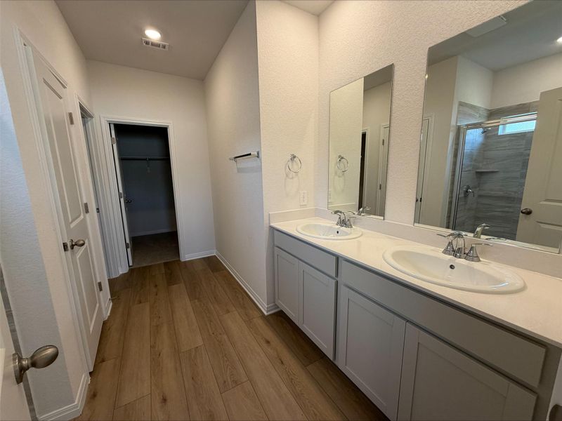 Full bathroom with a shower stall, light wood finished floors, double vanity, and a spacious closet Full bathroom with a shower stall, light wood finished floors, double vanity, and a spacious closet