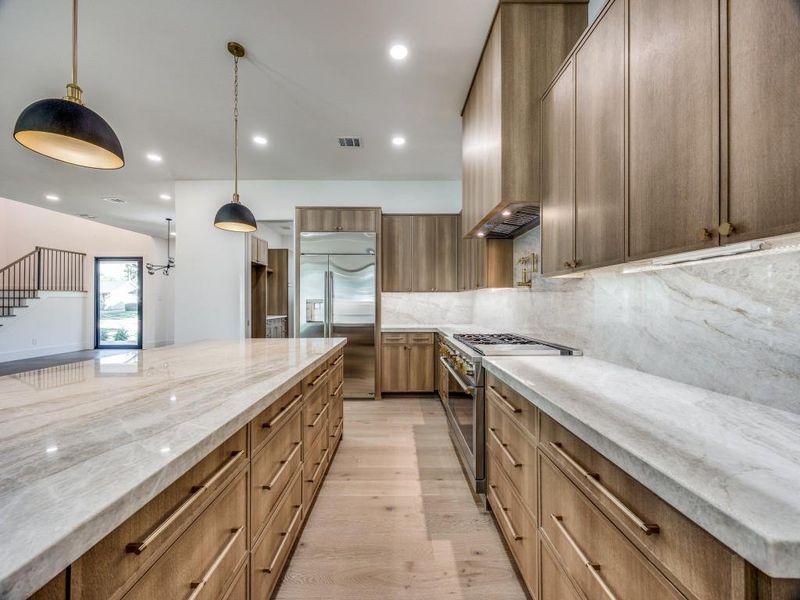 Kitchen featuring high end appliances, pendant lighting, backsplash, and light hardwood / wood-style flooring