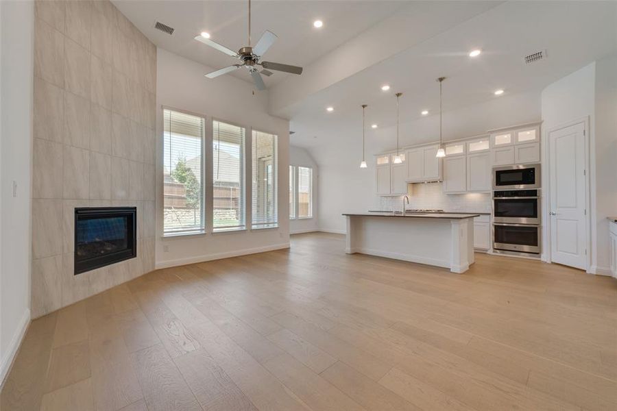 Kitchen featuring a kitchen island with sink, built in microwave, light hardwood / wood-style floors, hanging light fixtures, and stainless steel double oven