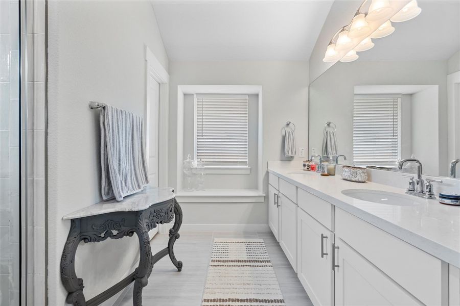 Full bathroom with double vanity, baseboards, a tile shower, and wood finished floors Full bathroom with double vanity, baseboards, a tile shower, and wood finished floors