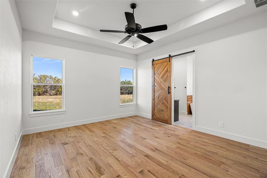 Master bedroom with light wood-type flooring, a barn door, multiple windows, and ceiling fan