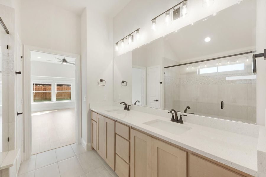 Master bathroom with double vanity, light wood cabinets, quartz countertops, and large mirror with overhead lighting