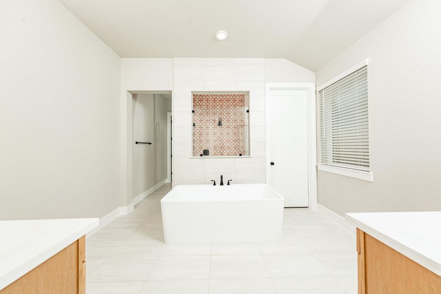 The centerpiece of this contemporary primary bath is the deep, freestanding bathtub with gorgeous tile flooring, offering an ideal spot for relaxation with a unique view into the walk-in shower.