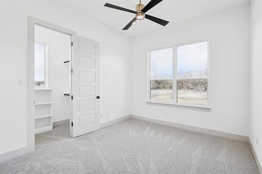 Unfurnished bedroom featuring light colored carpet, a ceiling fan, and a spacious closet Unfurnished bedroom featuring light colored carpet, a ceiling fan, and a spacious closet