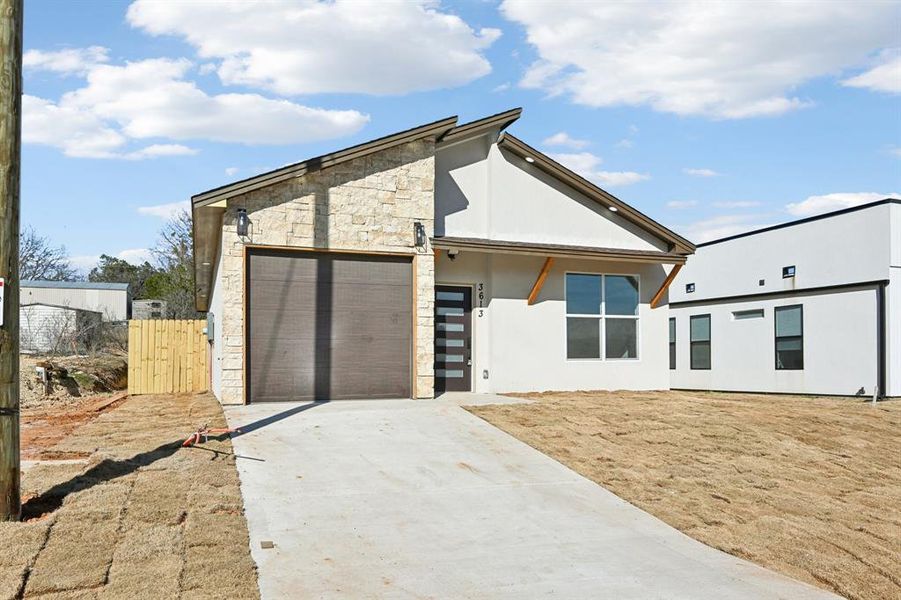 View of front facade with an attached garage, fence, stone siding, concrete driveway, and stucco siding